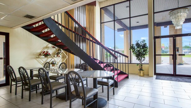 A dining area with a round table and chairs, a staircase with a red railing, and large windows with a view of the outside. - Rodeway Inn Bonifay (Bonifay)