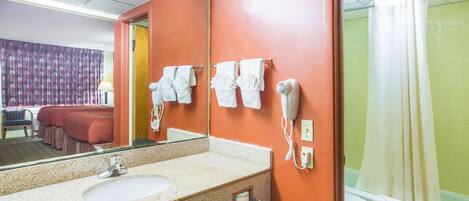 A hotel bathroom with a sink, mirror, towel rack, hairdryer, and a shower.