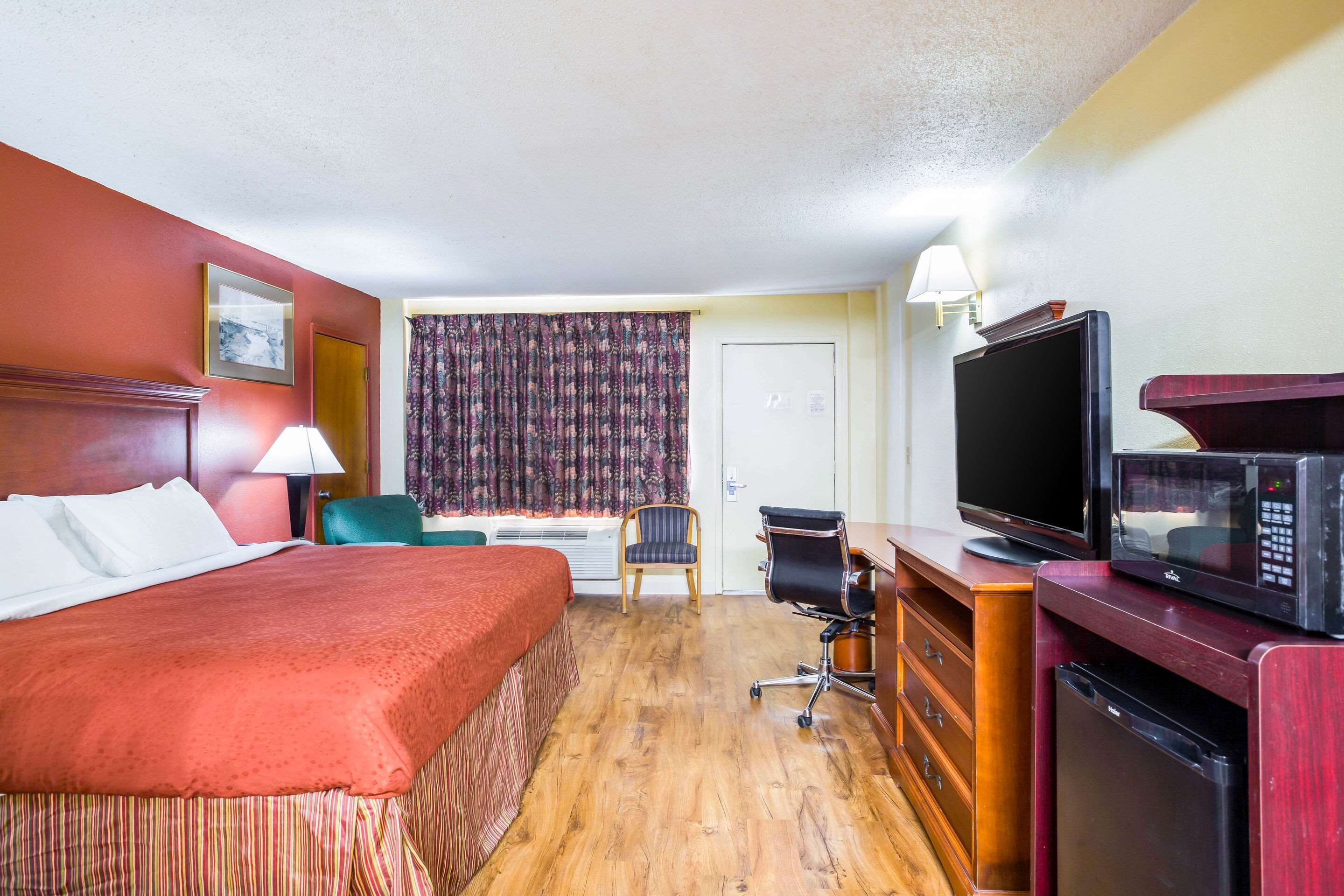 Ein Hotelzimmer mit Bett, Schreibtisch, Stuhl, Fernseher, Mikrowelle und kleinem Kühlschrank.