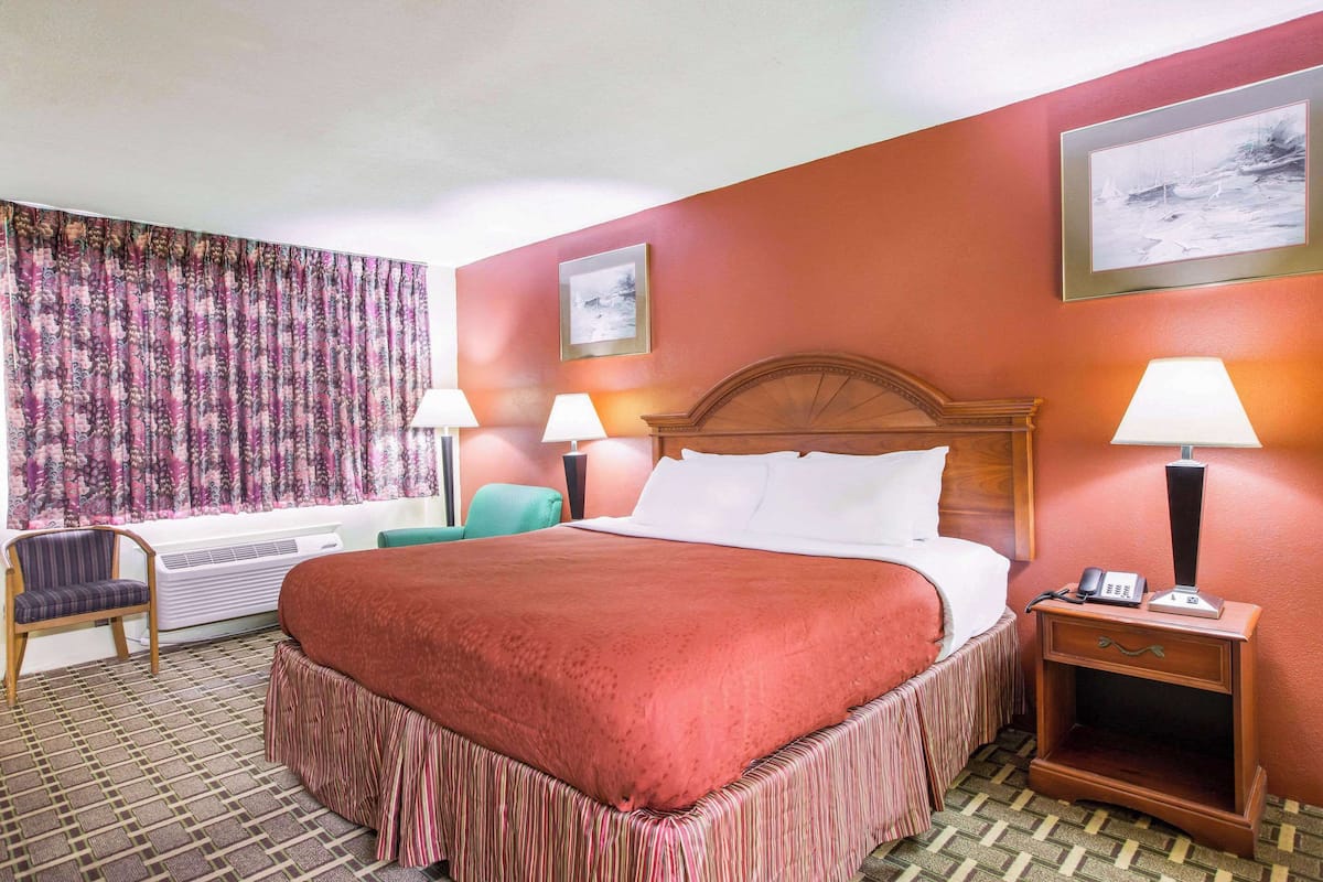 Camera d'albergo con un letto grande, due abat-jour, un comodino con un telefono, una sedia e una finestra con tende.