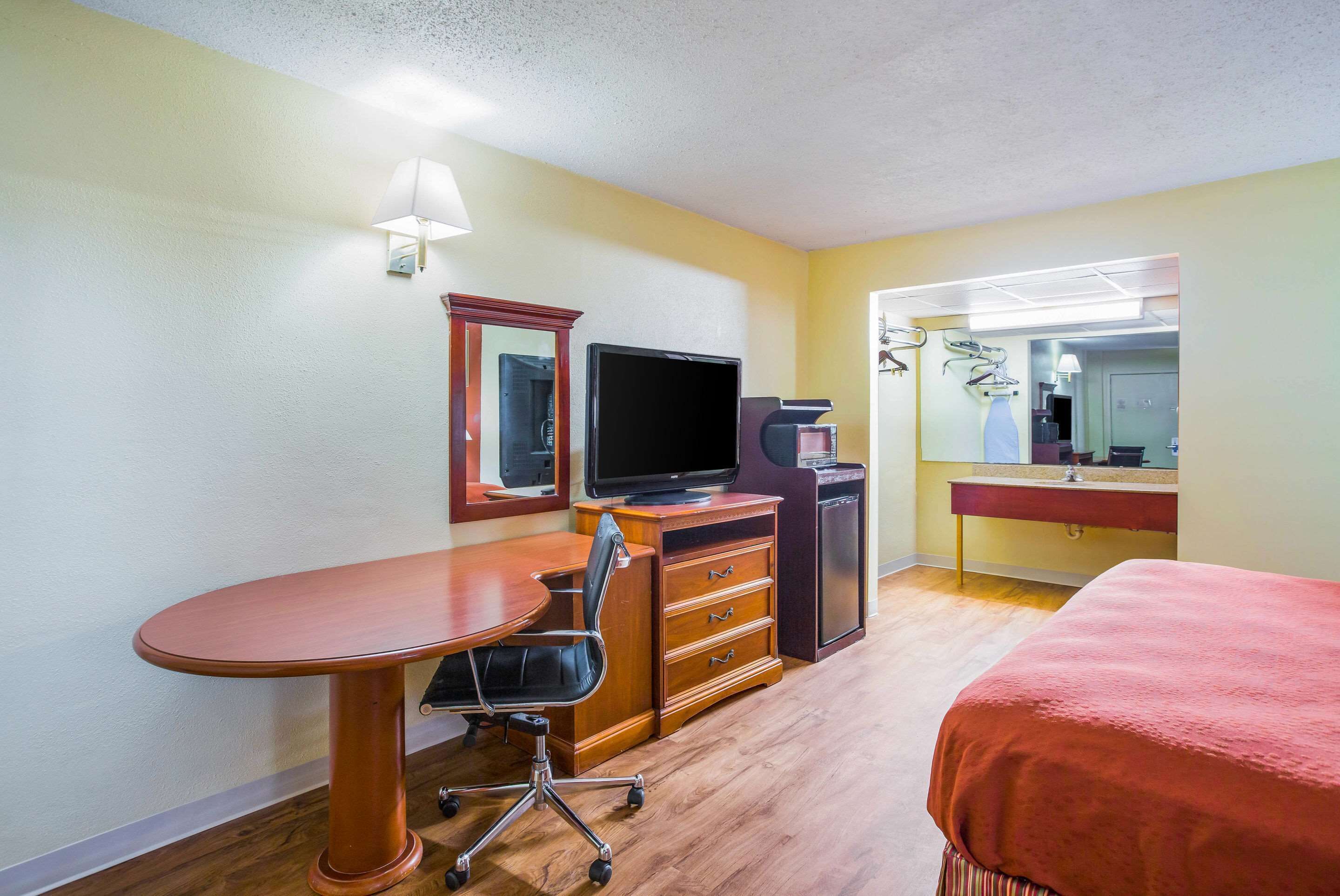 A hotel room with a wooden desk, a television, a mirror, and a bed.