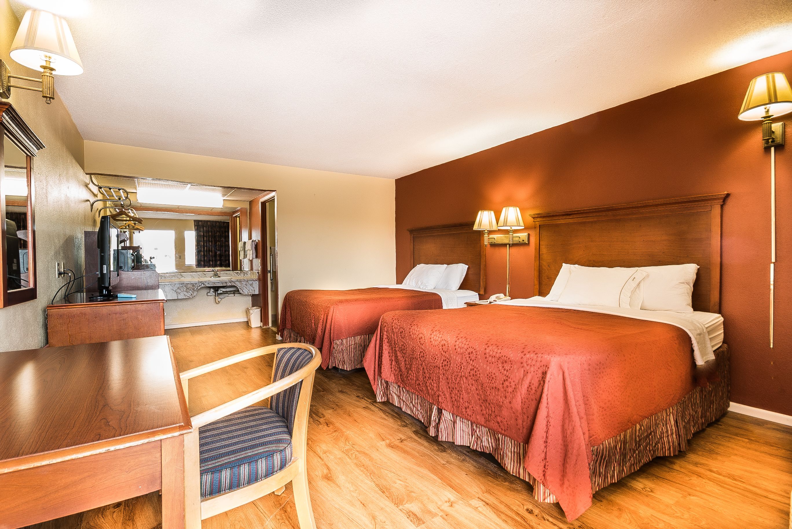 A hotel room with two beds, a desk, a chair, and a kitchenette.