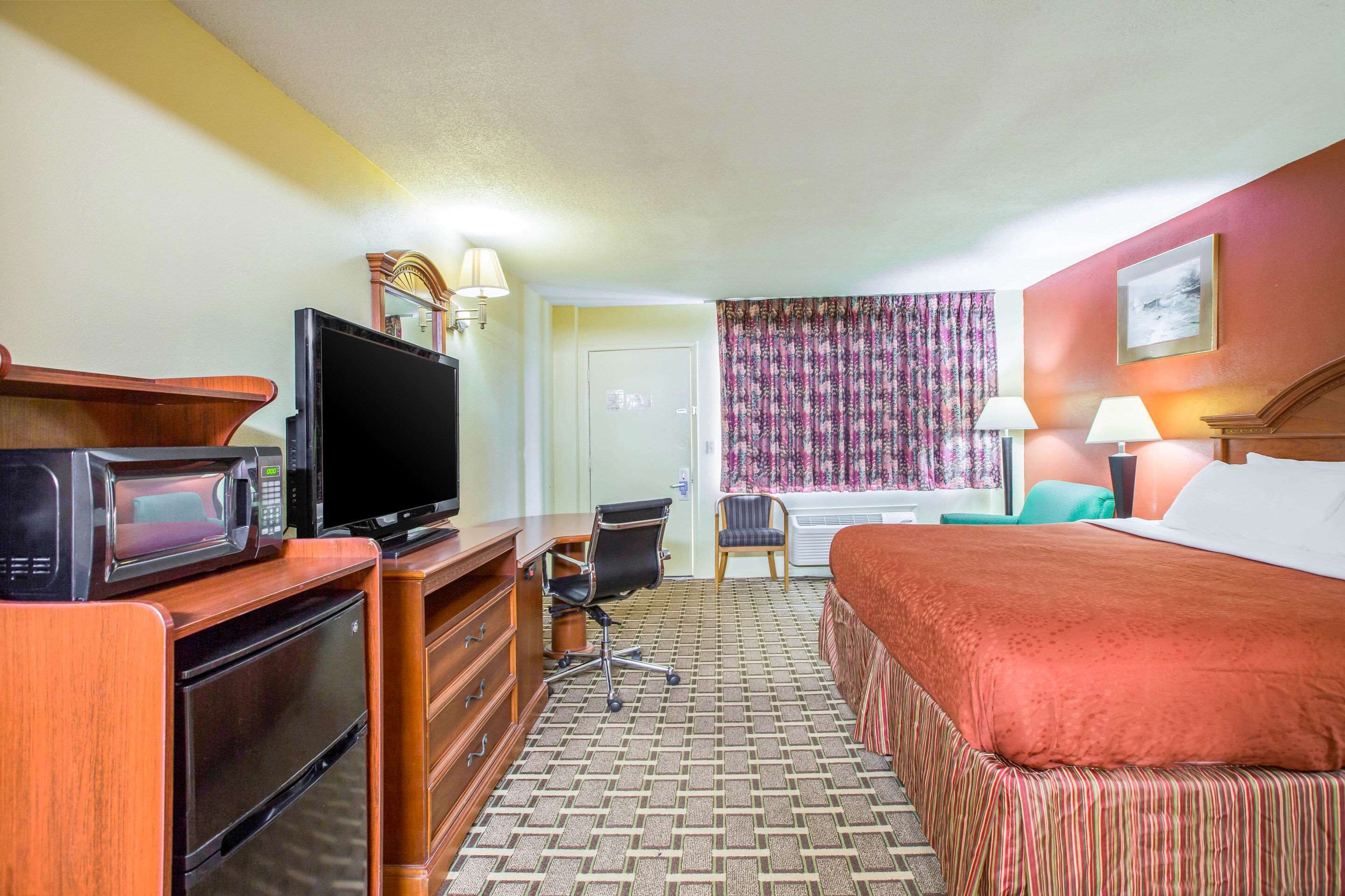 Quarto de hotel com cama, escrivaninha, computador, televisão e micro-ondas.
