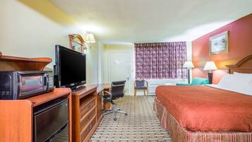 Quarto de hotel com cama, escrivaninha, computador, televisão e micro-ondas.