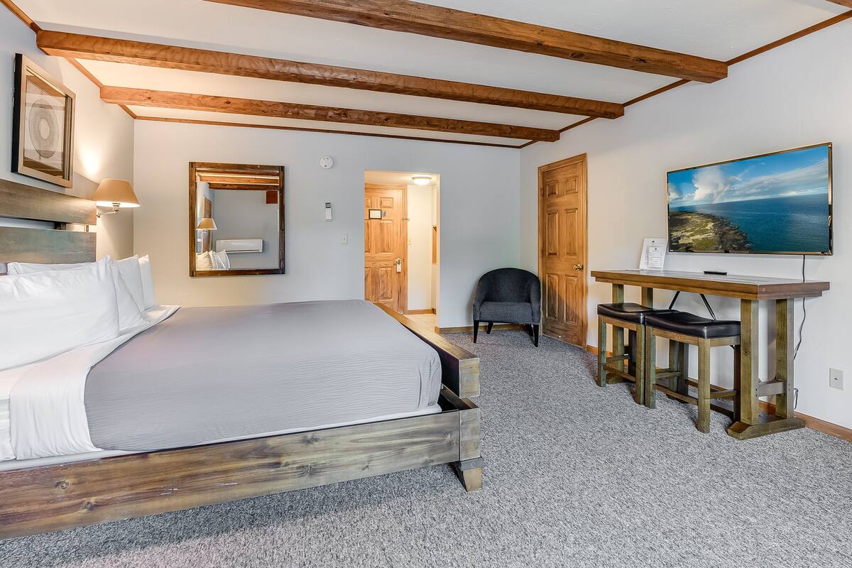 A bedroom with a bed, a desk, a chair, a TV, and a door leading to another room.