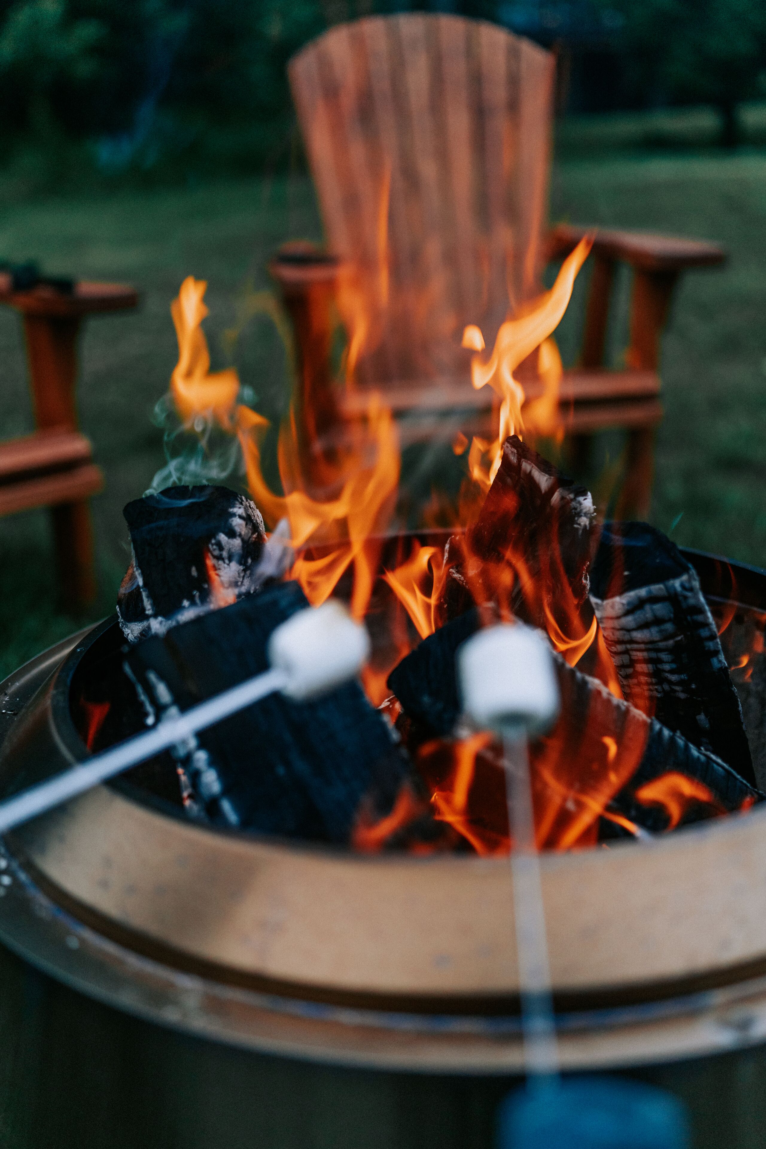 A fire pit with logs and marshmallows, surrounded by wooden chairs.