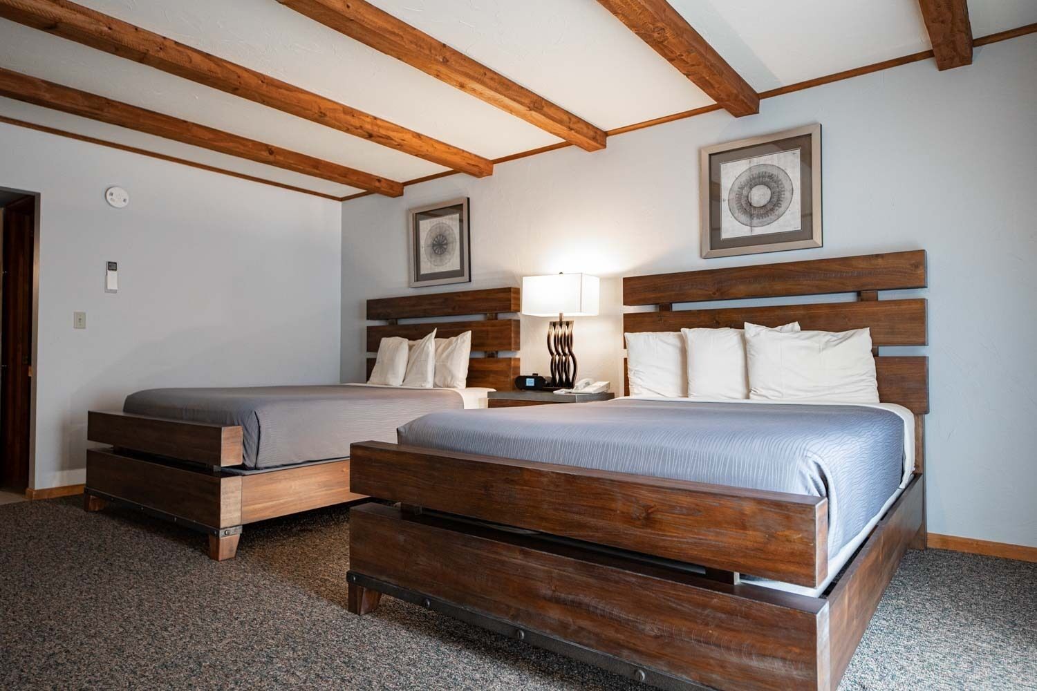 Una habitación de hotel con dos camas de madera, una mesita de noche con una lámpara y un cuadro enmarcado en la pared.