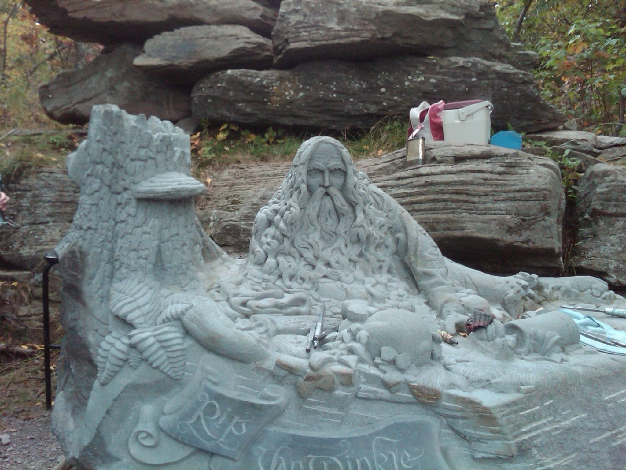 A stone sculpture of a figure with a beard, surrounded by rocks and foliage.