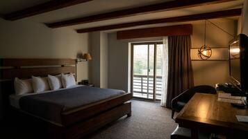 Quarto de hotel com cama de madeira, escrivaninha e uma grande janela com cortinas.