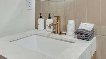 Et badeværelsesvask med bordplade i marmor, en guldfarvet vandhane og toiletartikler, herunder en lotionflaske og en sæbeflaske.