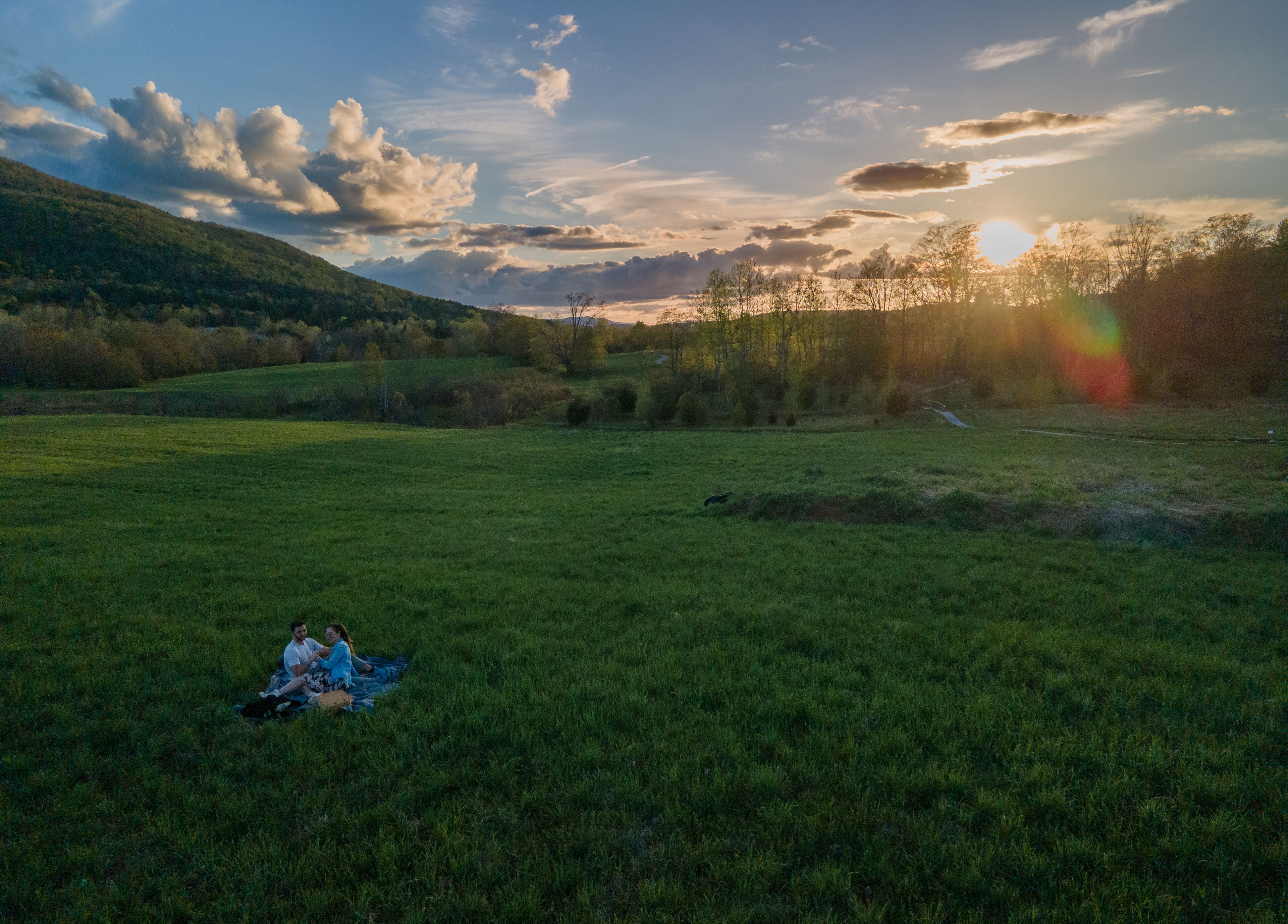 A grassy field with a person sitting on a blanket.