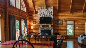 A cozy cabin interior with a stone fireplace, wooden walls, a dining area with a red and black checkered tablecloth, and a television mounted above the fireplace. - Hotel Vienna (Windham)