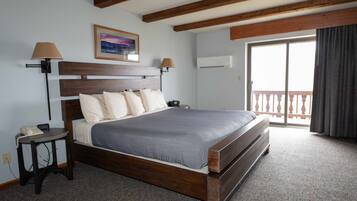 Habitación de hotel con cama de madera, una mesita de noche, una lámpara, un cuadro en la pared y un balcón con vistas.