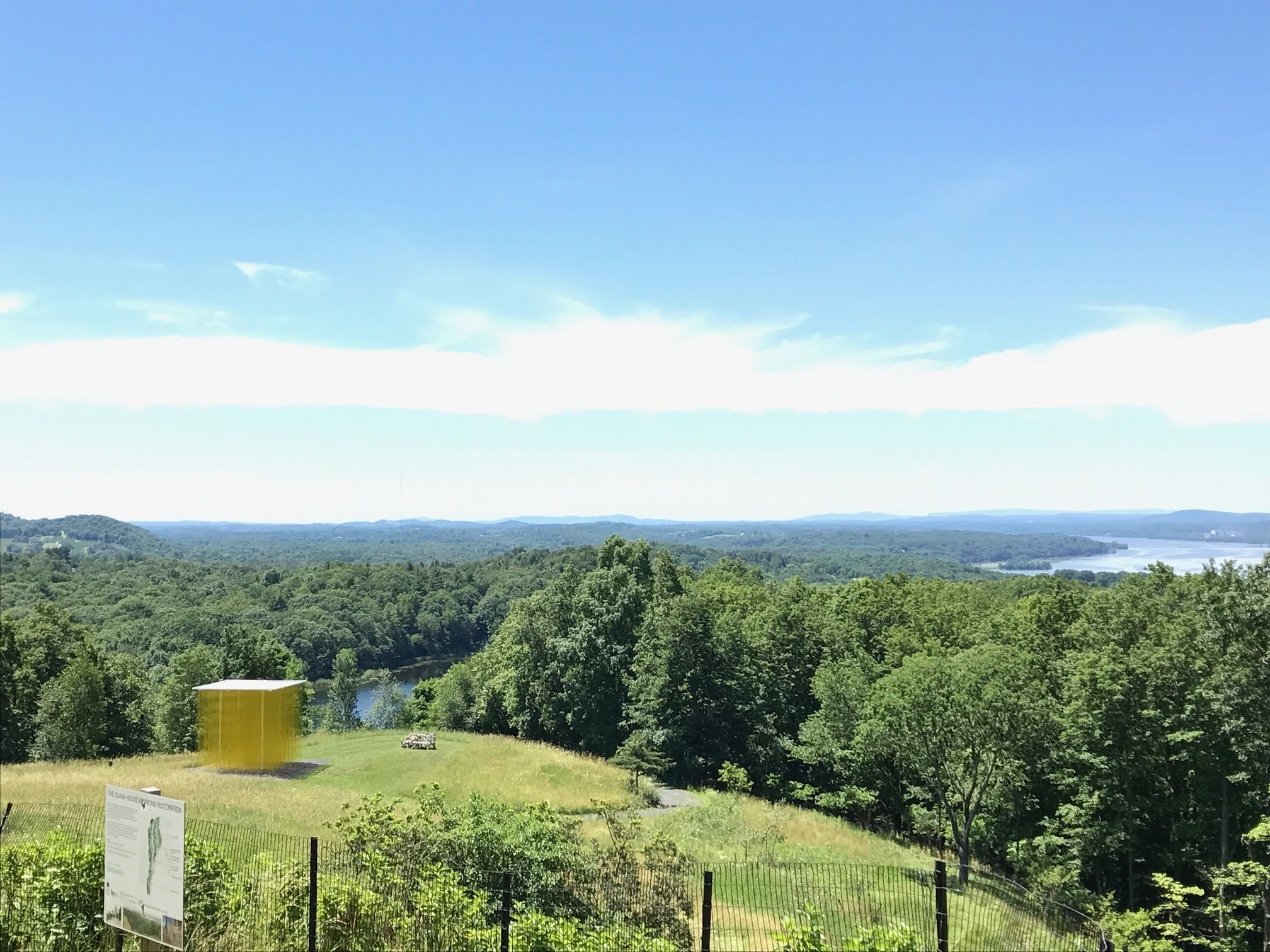 A lush green landscape with a fenced area, a yellow structure, and a signboard.