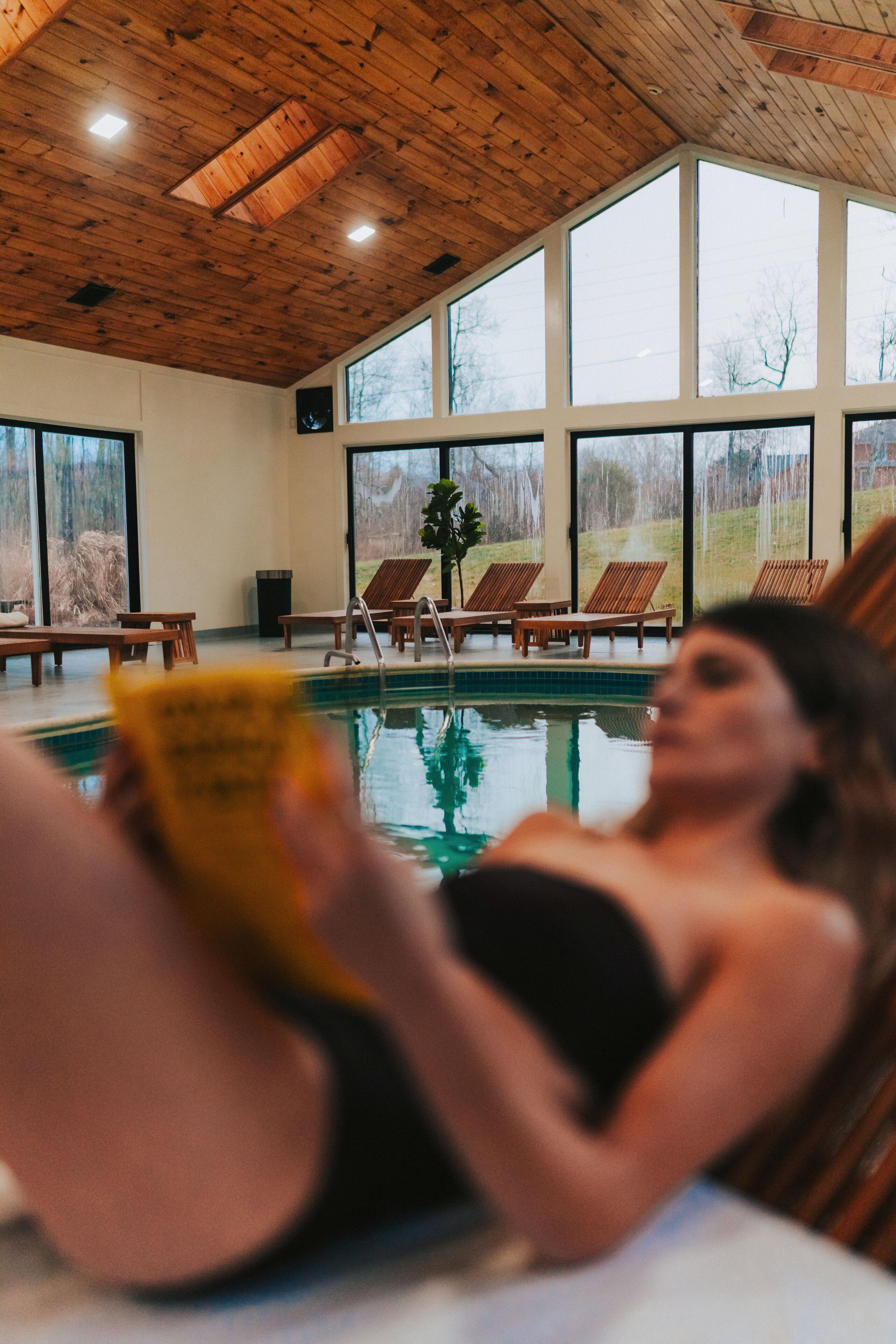 A pool area with wooden deck chairs and a person reading a book.