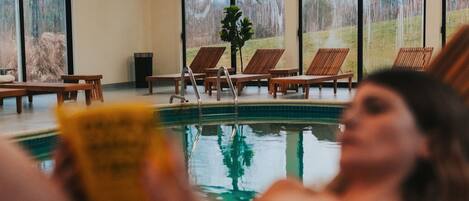 A pool area with wooden deck chairs and a person reading a book.