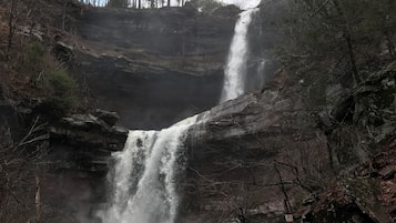 Una cascada se precipita sobre terreno rocoso, rodeada de árboles.