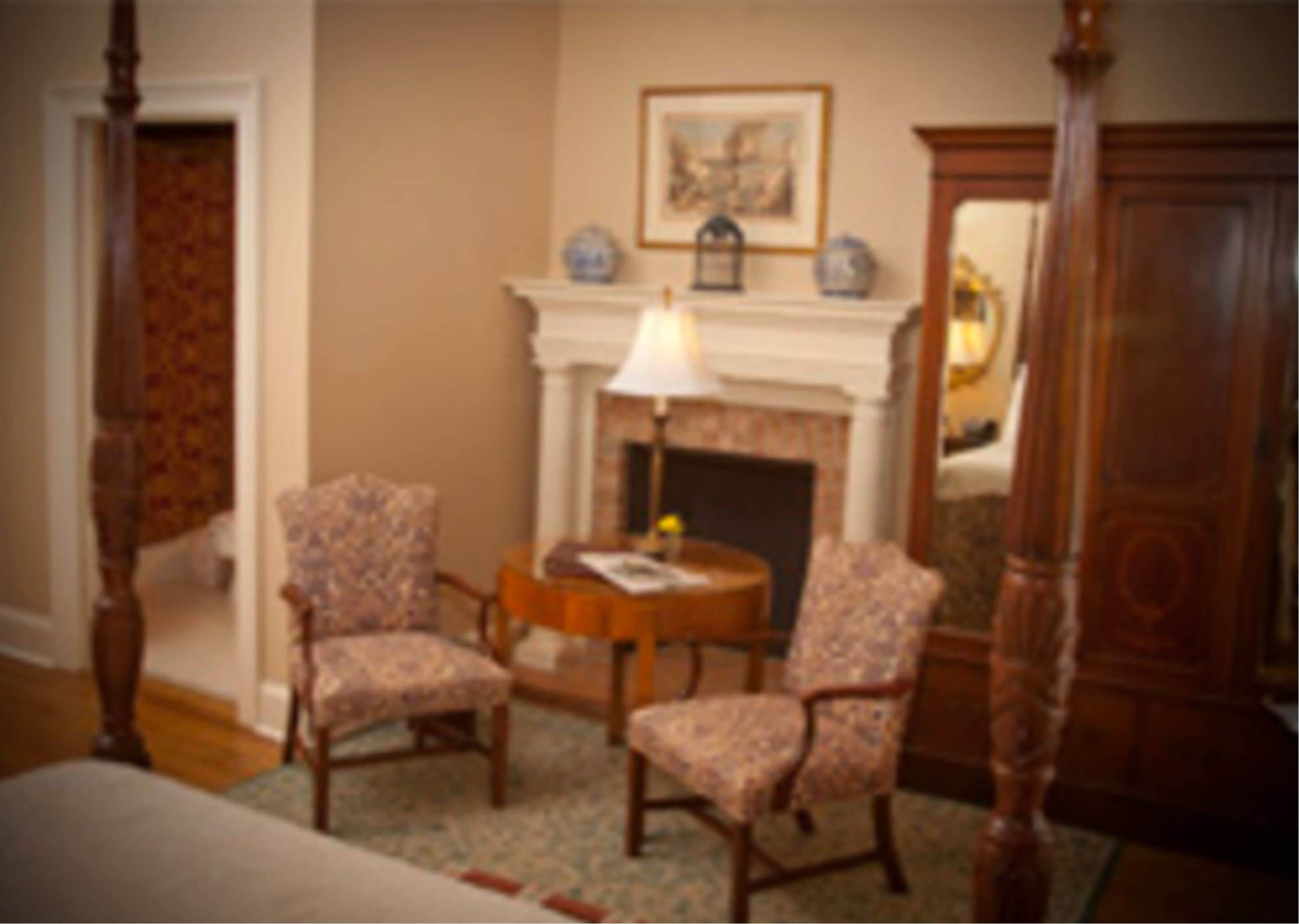 A room with a fireplace, two armchairs, a round table, and a mirror.