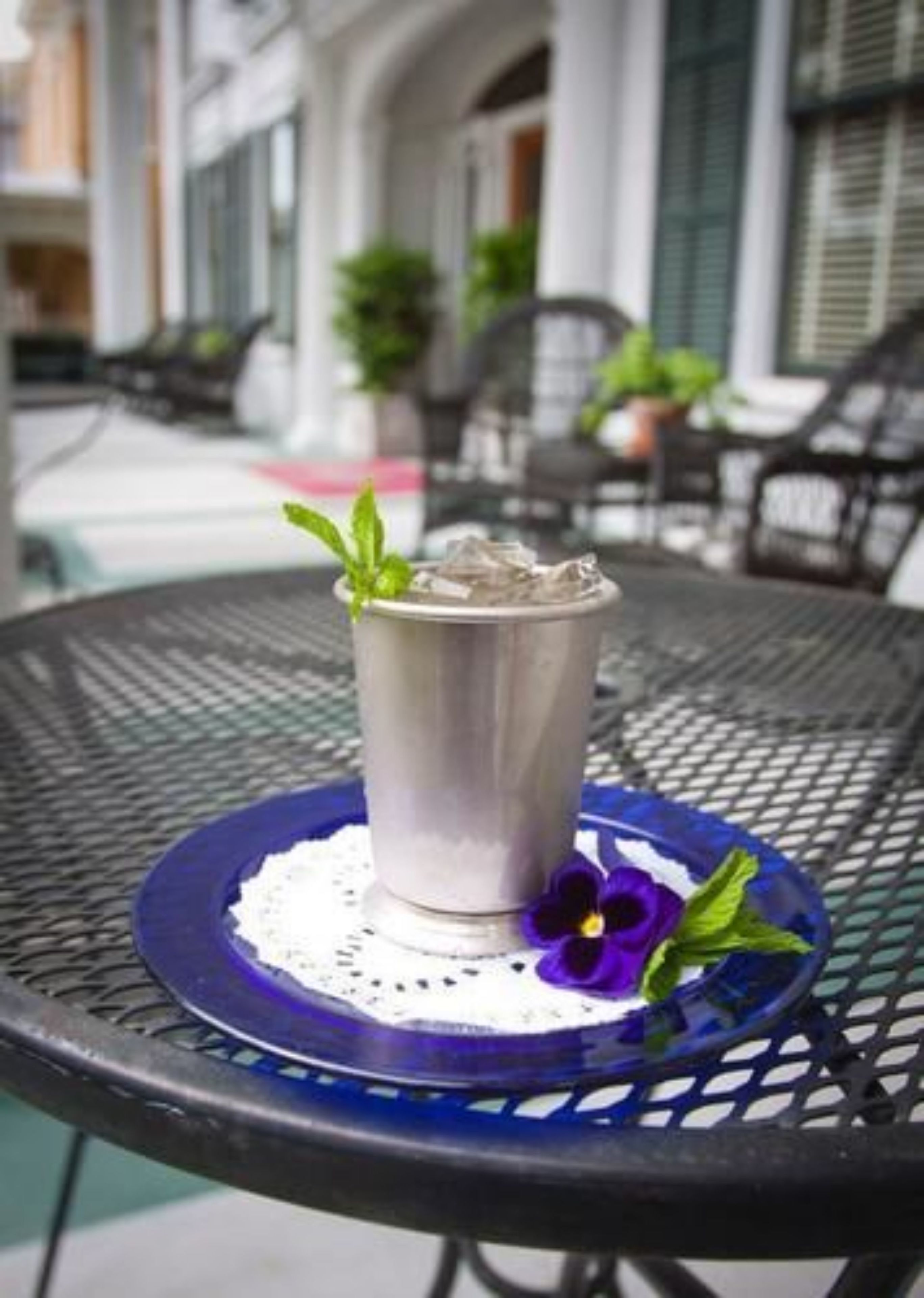 A metallic cup with a mint garnish on a blue coaster, placed on a round metal table outdoors.