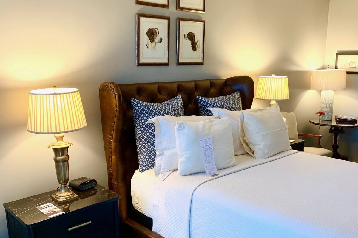 A neatly made bed with a headboard, two bedside tables with lamps, and framed pictures on the wall.