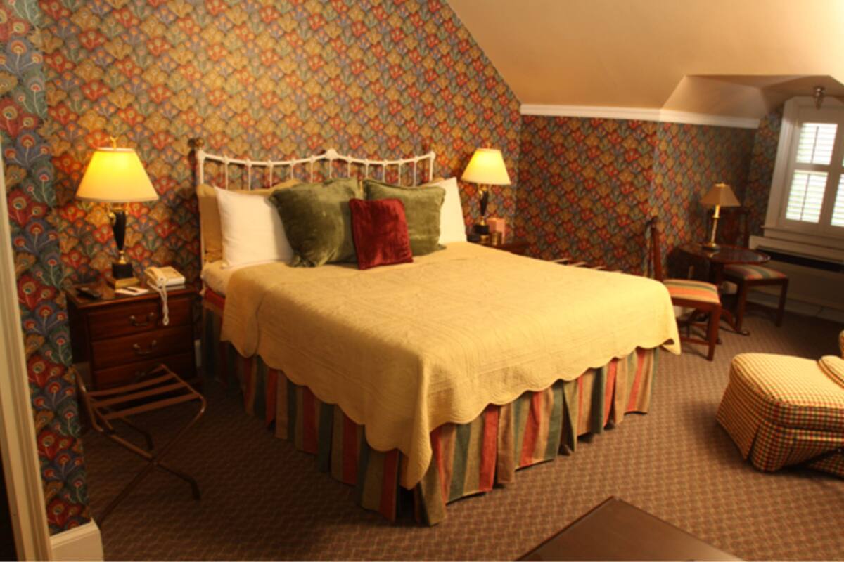 A bedroom with a bed, two bedside tables, a nightstand, a chair, and a window.
