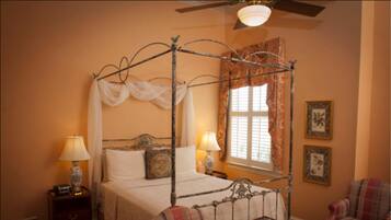 A four-poster bed with a canopy, two bedside lamps, a nightstand, a chair, and a small table with a book.