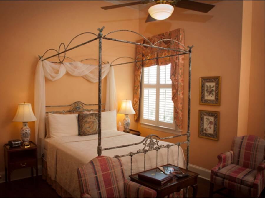 A four-poster bed with a canopy, two bedside lamps, a nightstand, a chair, and a small table with a book.