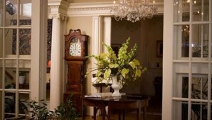Una habitación con candelabro, un reloj y una mesa con un jarrón de flores.