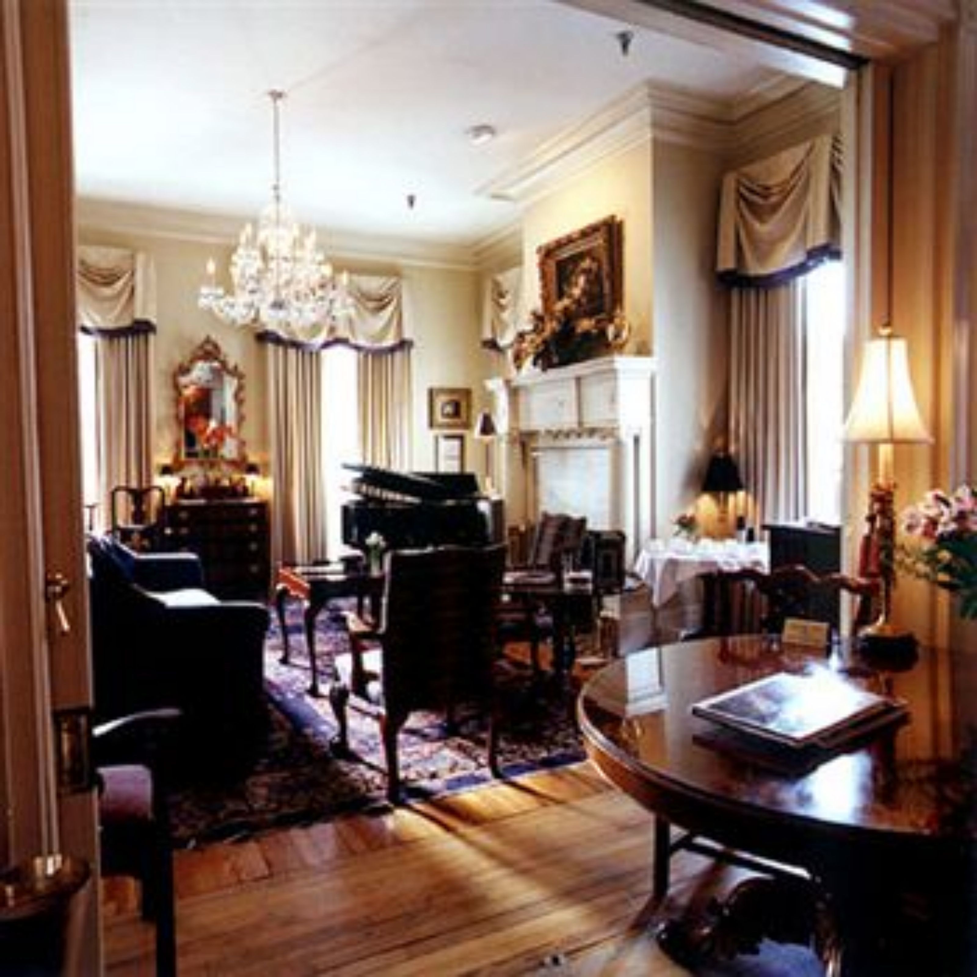 A formal living room with a grand piano, a chandelier, and a fireplace.