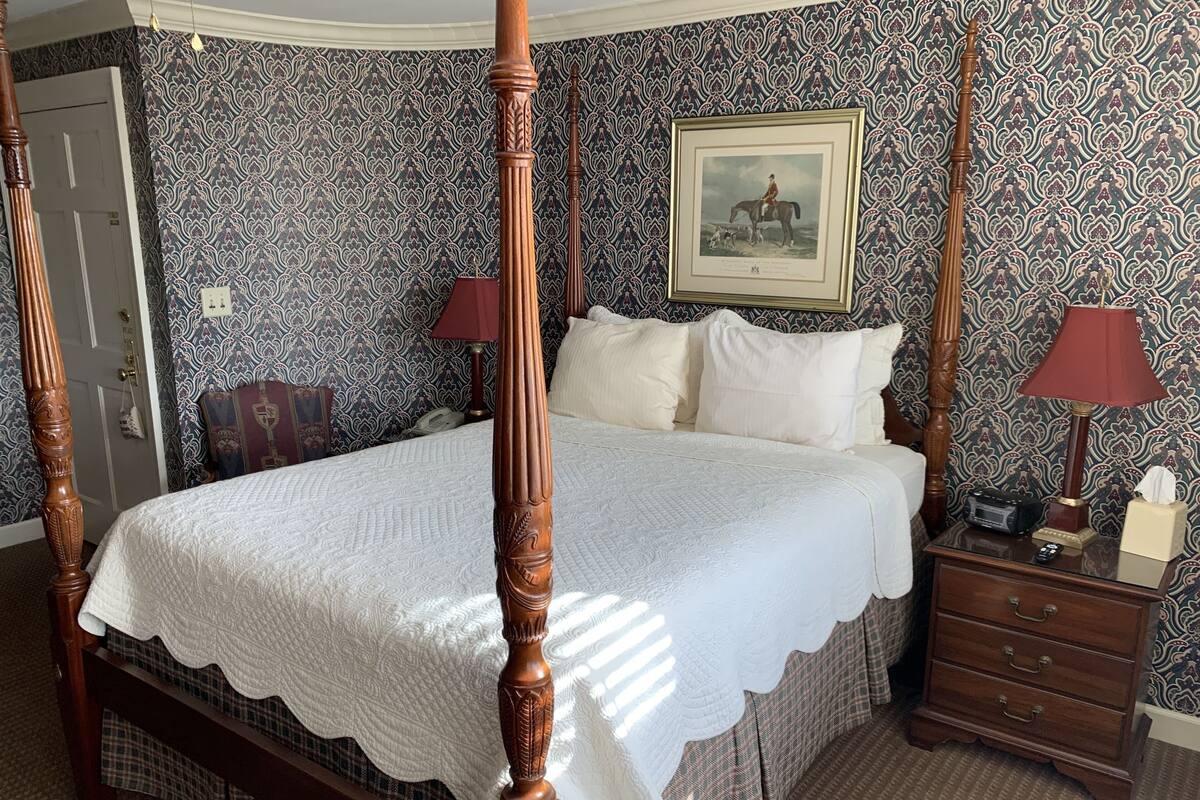 A four-poster bed with a white quilt, a nightstand with a lamp, and a framed picture on the wall.