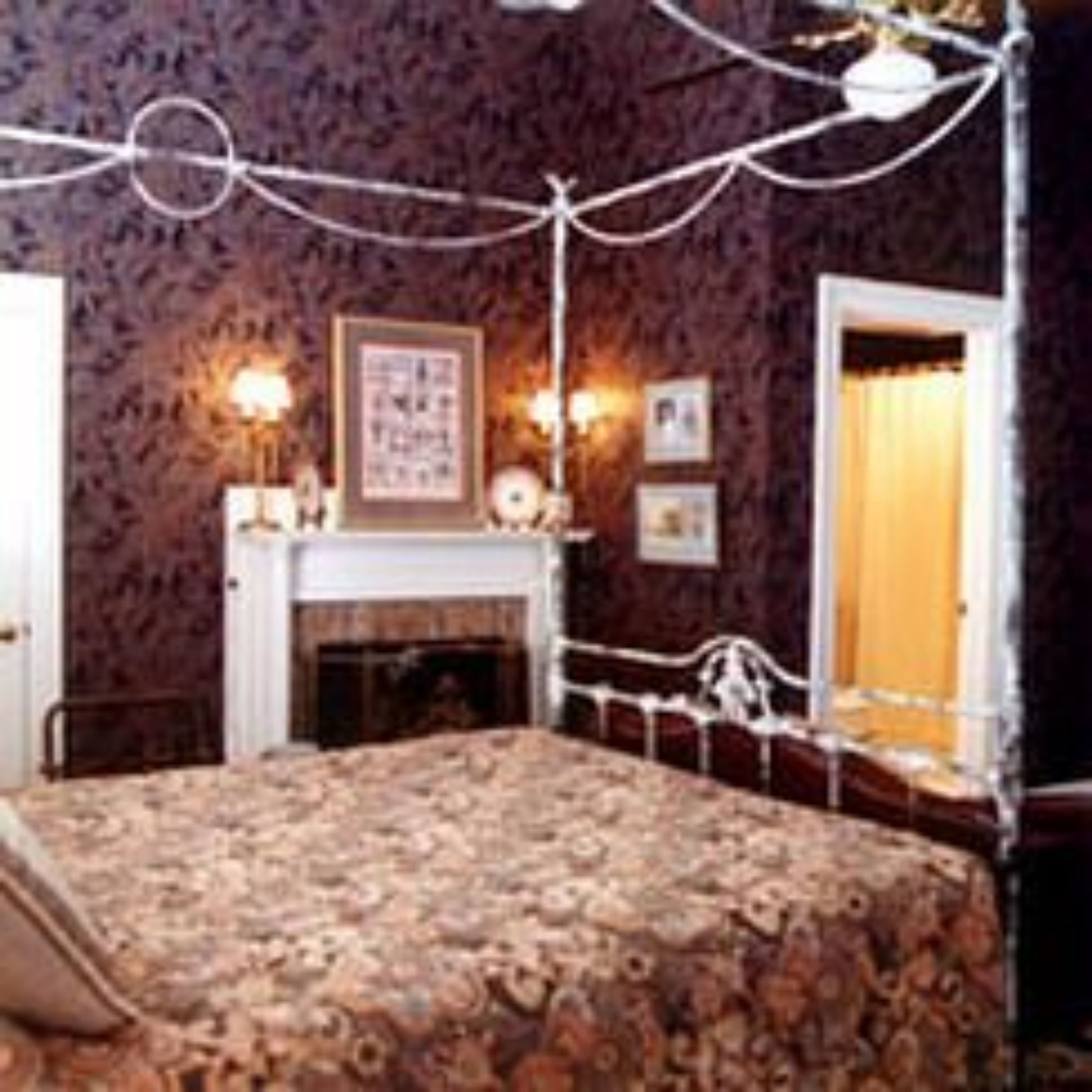 A bedroom with a floral bedspread, a fireplace, and wall-mounted lights.