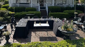 Una casa de dos pisos con un porche delantero, un comedor con mesas dispuestas para cuatro personas y un jardín bien cuidado.
