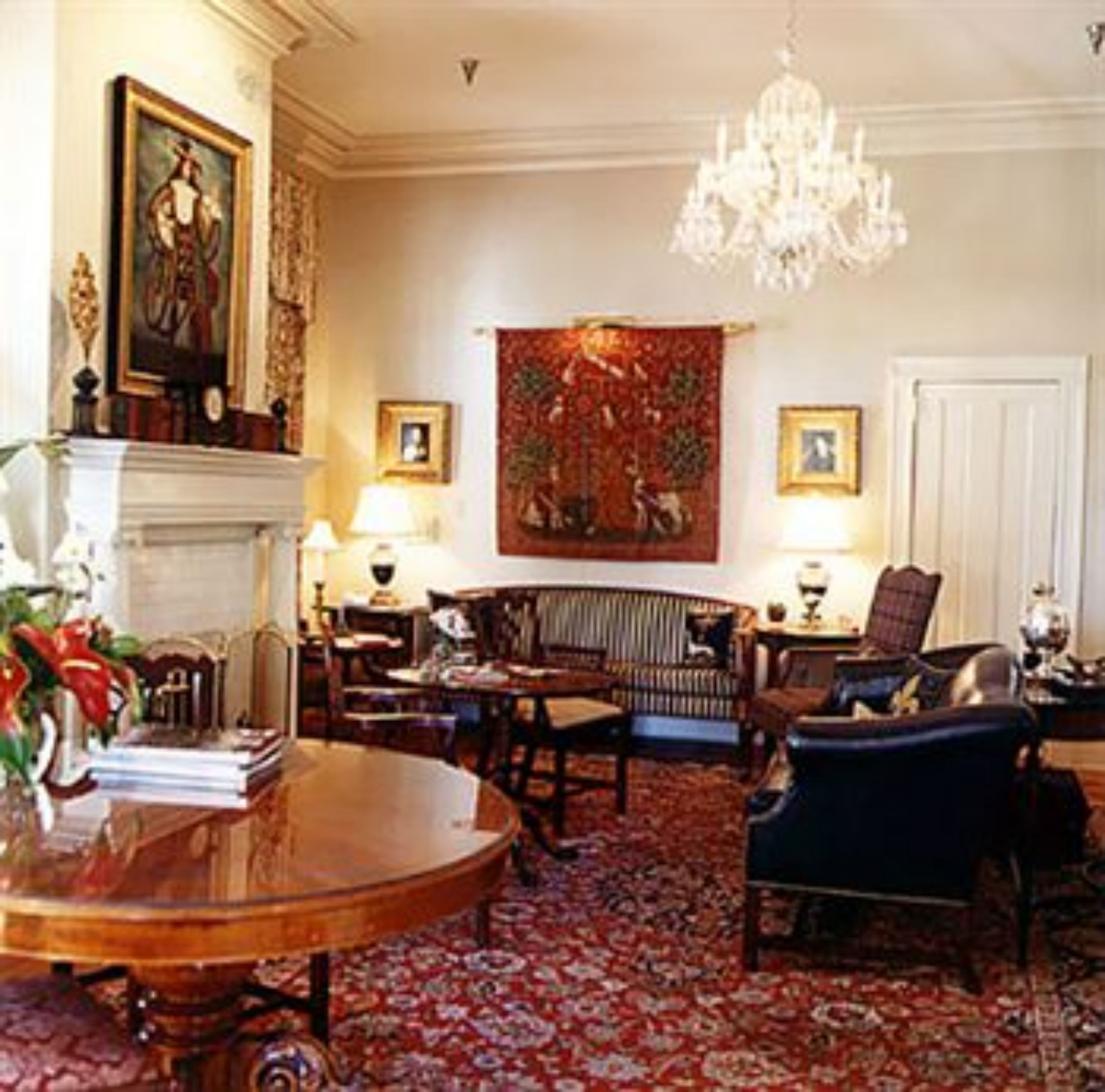 Uma sala de estar formal com lareira, um candelabro e um tapete vermelho estampado.
