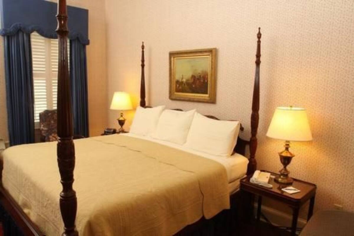 A four-poster bed with a beige bedspread, two bedside lamps, and a framed picture on the wall.