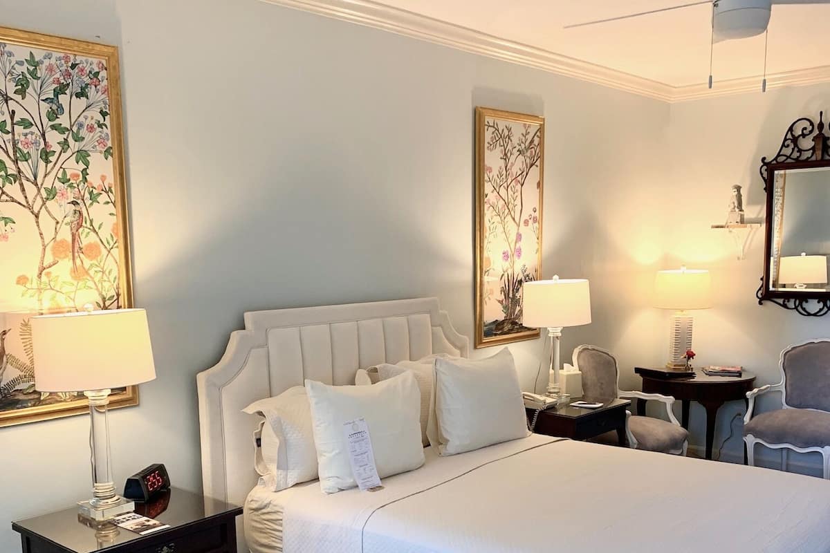 A hotel room with a large bed, two bedside tables, a ceiling fan, and artwork on the walls.