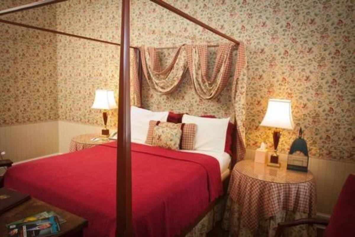 A bedroom with a four-poster bed, floral wallpaper, and a round table with a lamp.