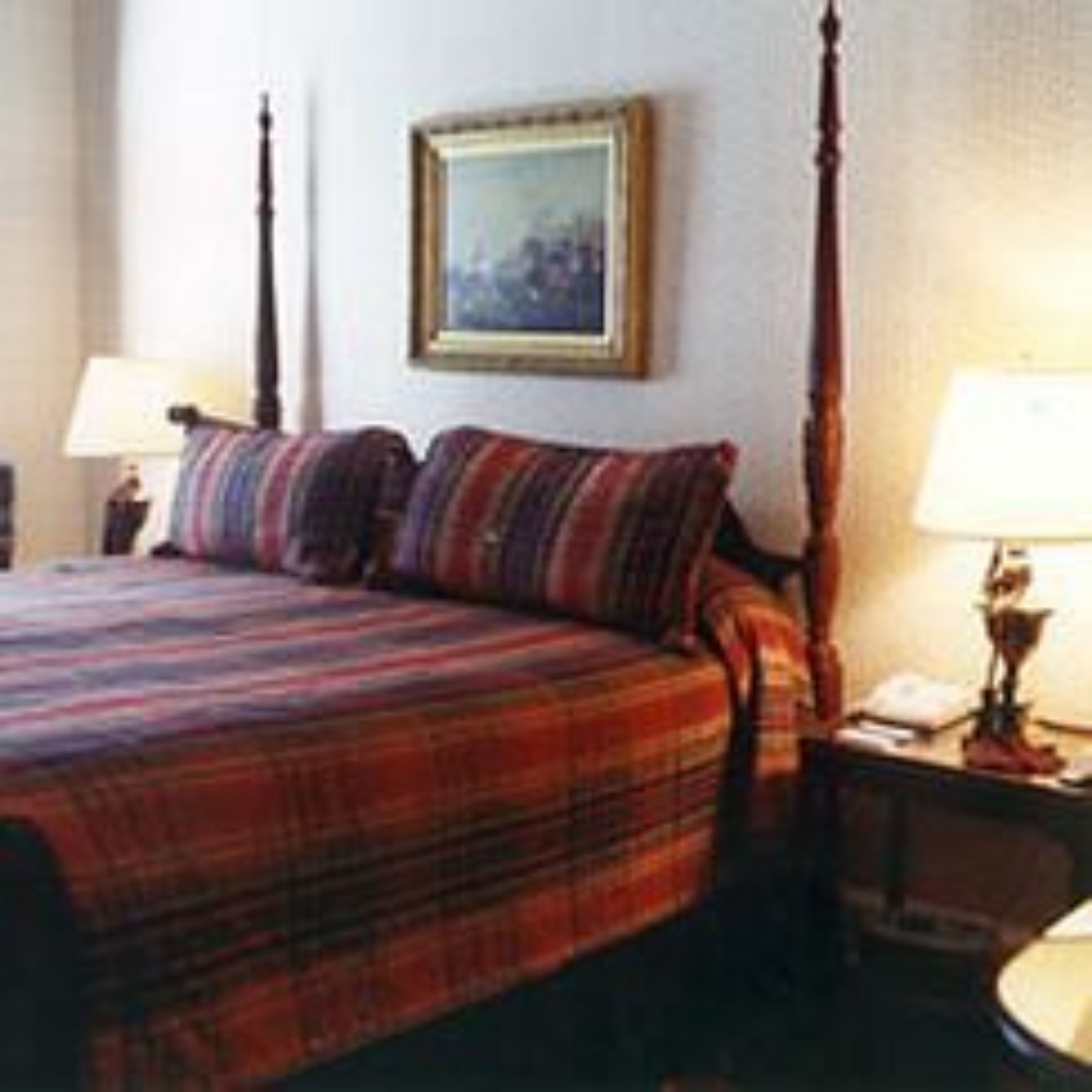 A hotel room with a four-poster bed, a framed picture on the wall, and a bedside table with a lamp.