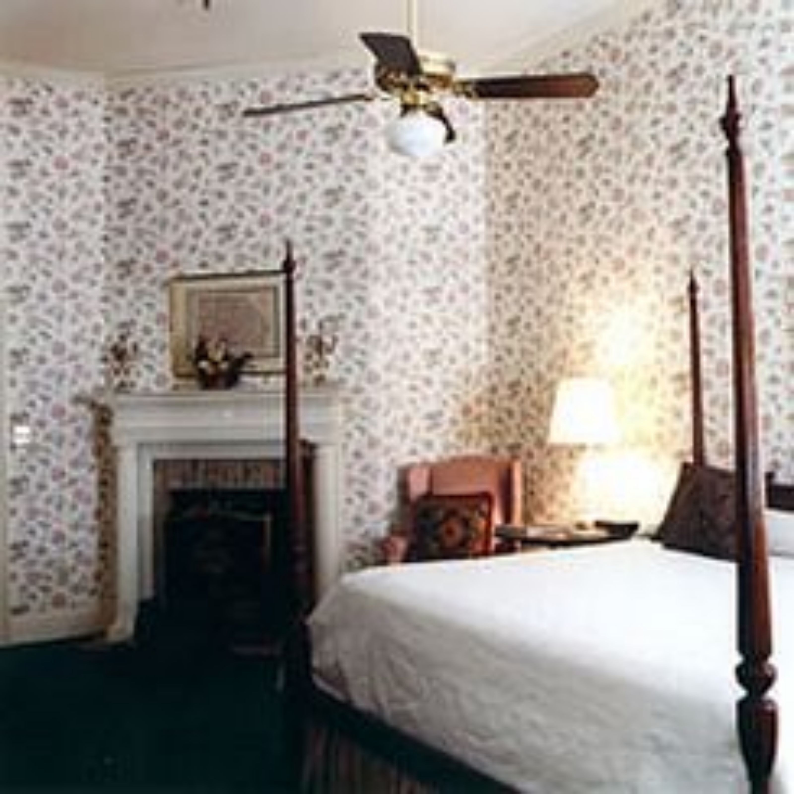 A bedroom with a four-poster bed, a fireplace, and a ceiling fan.