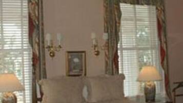 A bedroom with a bed, two bedside tables, a nightstand, and a window with curtains.