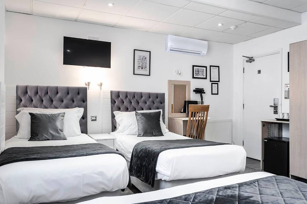 A hotel room with two beds, a flat-screen TV, air conditioning, framed pictures, a desk, and a small kitchenette.
