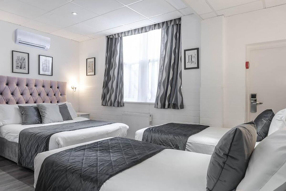 A hotel room with a large bed, two smaller beds, a tufted headboard, and a window with curtains.