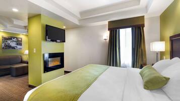 Une chambre d’hôtel avec un grand lit, un téléviseur à écran plat fixé au mur, une cheminée, un canapé et une fenêtre avec des rideaux.