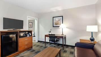 A hotel room with a flat-screen TV, a wooden desk, a chair, a sofa, a coffee table, and a lamp.