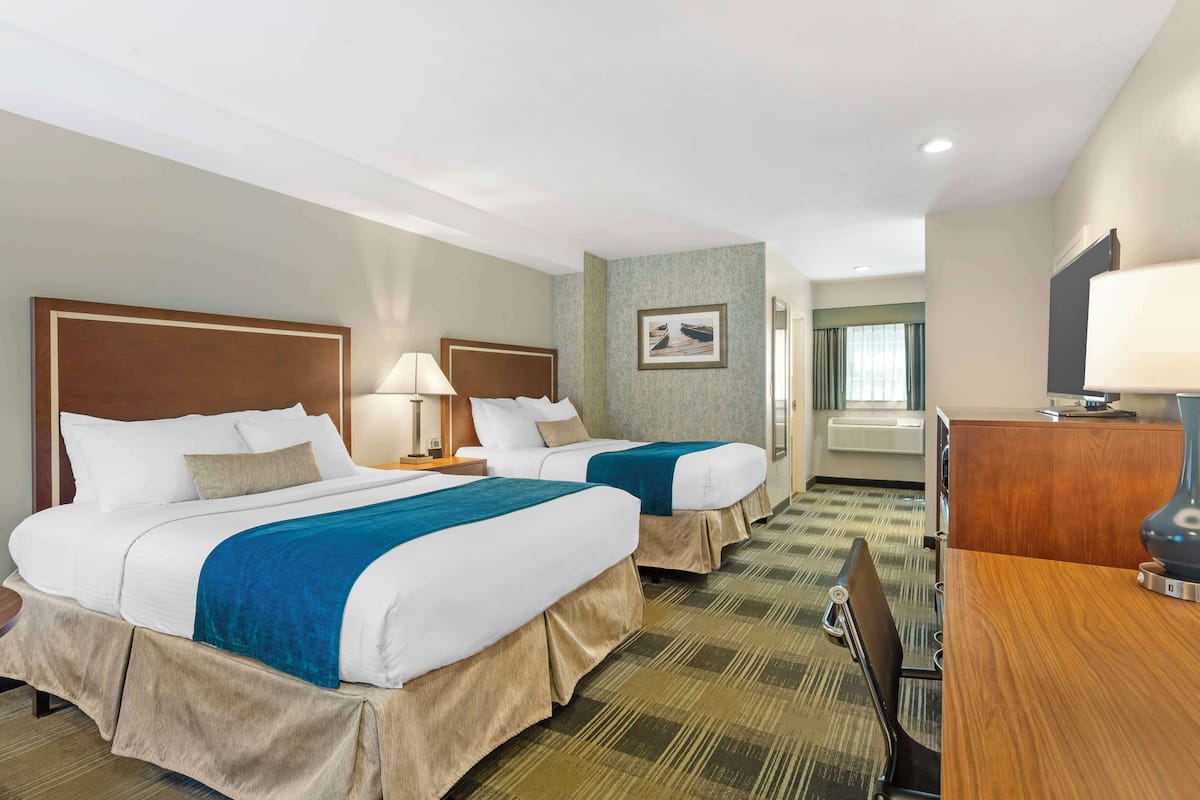 A hotel room with two beds, a desk, a chair, a TV, and a picture on the wall.