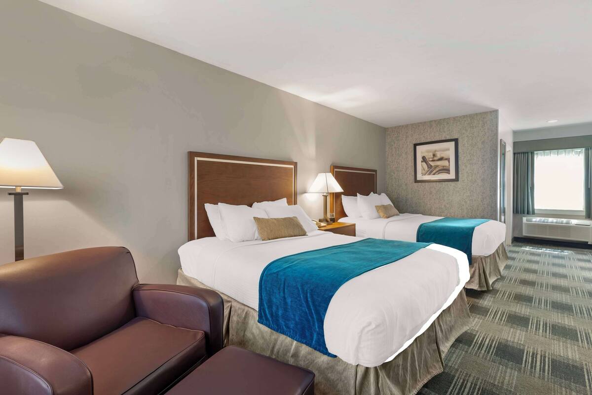 A hotel room with two beds, a sofa, a lamp, and a picture on the wall.