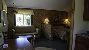 A compact room with a sofa, a small dining table, a bed with a patterned bedspread, and a kitchenette area. - Kennebunk Gallery Motel & Cottages (Kennebunk)