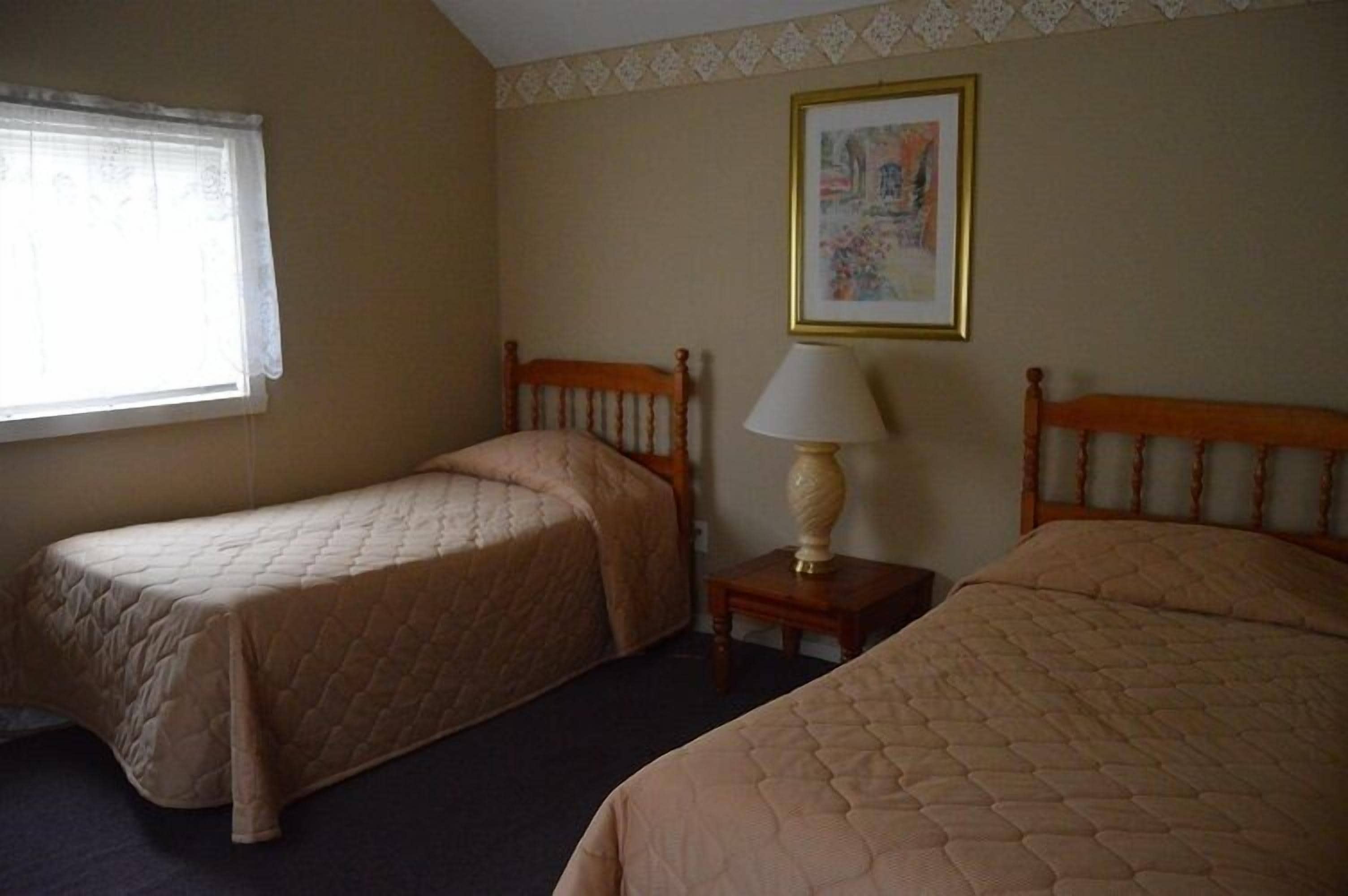 A room with two single beds, a small table with a lamp, and a framed picture on the wall.