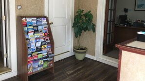 A hallway with a wooden rack of travel brochures, a potted plant, a clock on the wall, and a door leading to another room. - Kennebunk Gallery Motel & Cottages (Kennebunk)