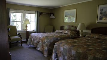 A hotel room with two beds, a chair, a desk with a lamp, and a window with curtains.