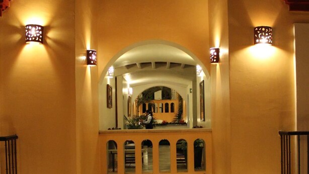 A corridor with arched ceilings and wall-mounted lights, leading to a balcony with a railing.